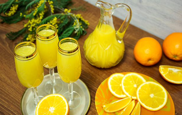Mimosa servi dans une flûte à champagne avec oranges tranchées et pichet de jus d’oranges sur la table