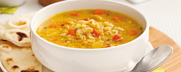 Un bol de soupe au bouillon orangé avec légumes en cubes, orge et lentilles.