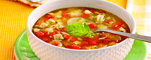 Bol rempli de soupe avec morceaux de poulet, légumes et feuilles de basilic sur le dessus.