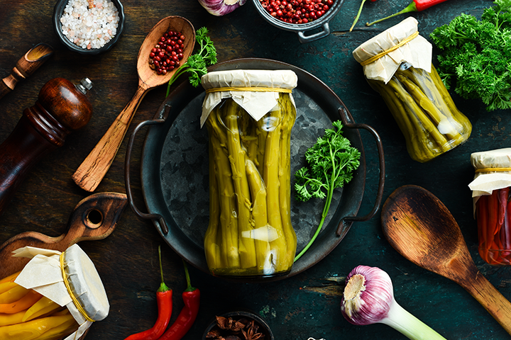 Asperges vertes marinées dans un pot en verre sur une table remplie d'aromates