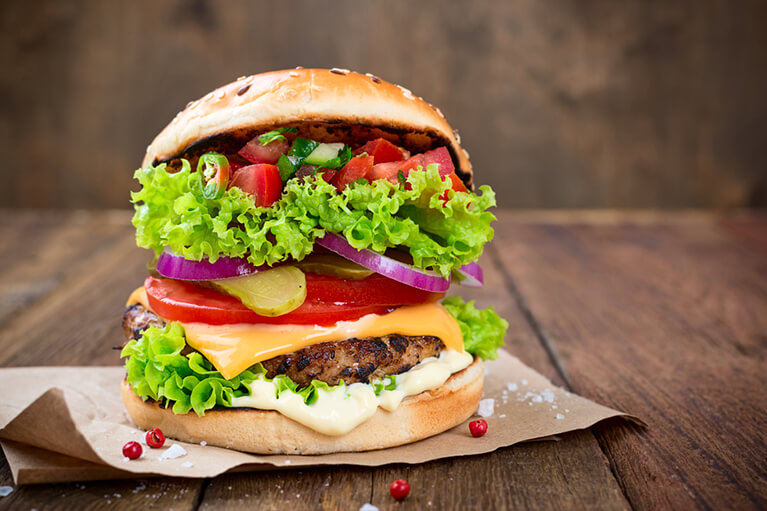 Un gros burger rempli d'ingrédients comme des tomates, de la salade, des oignons et de la salsa pour ajouter du piquant.
