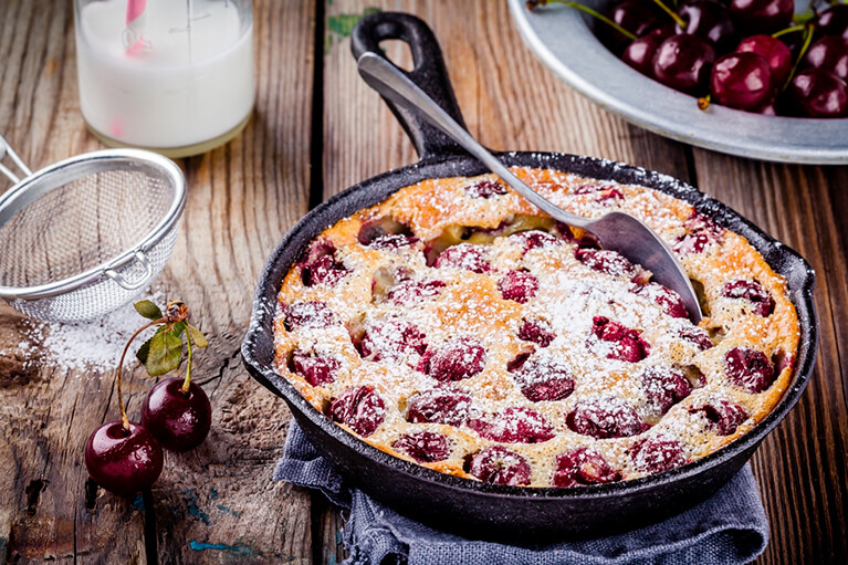 Un clafoutis végétalien aux cerises saupoudré de sucre à glacer sur un fond de bois rustique