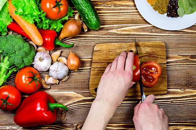 Des mains coupent des légumes sur une planche de bois