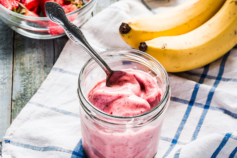 Un pot en verre contenant de la crème glacée végétalienne sans produits laitiers, le tout entouré de fruits santé comme des bananes et des fraises.