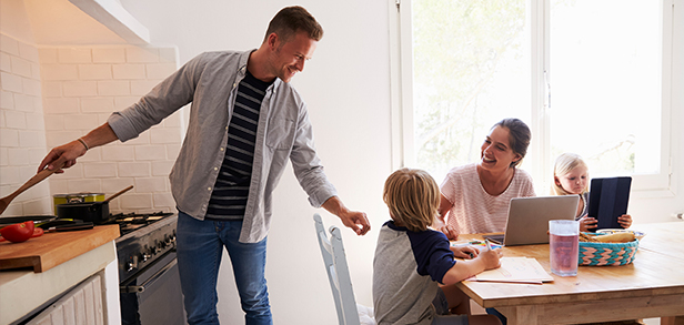 Un père cuisine pendant que la mère aide les enfants avec les devoirs