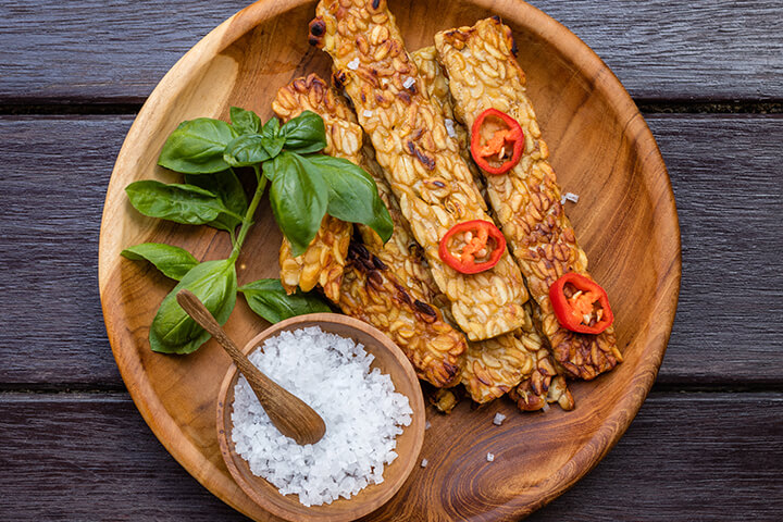 Frites de tempeh dans une assiette en bois avec des feuilles de basilic et du sel