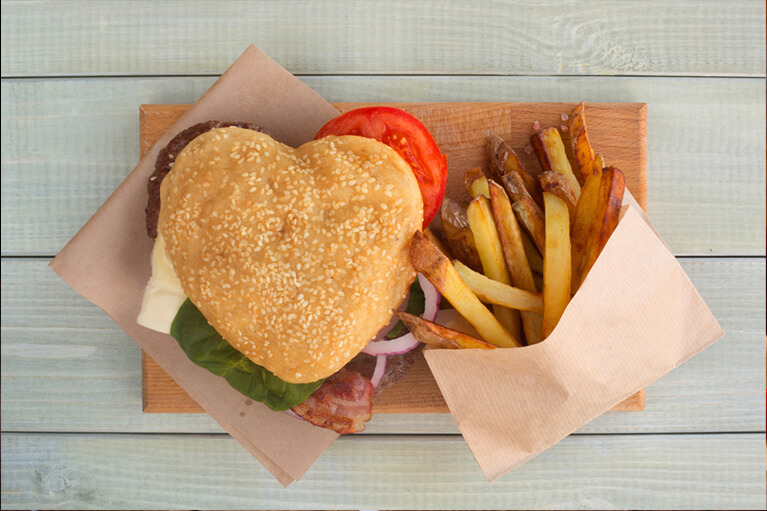 Un hamburger épicé romantique en forme de cœur accompagné de frites sur une planche en bois
