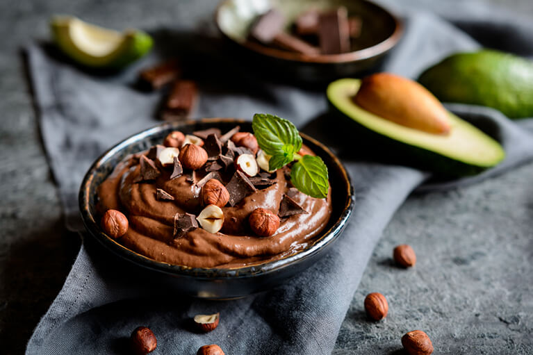 Une mousse au chocolat végane onctueuse accompagnée d'un avocat ouvert en deux et décorée de noisettes