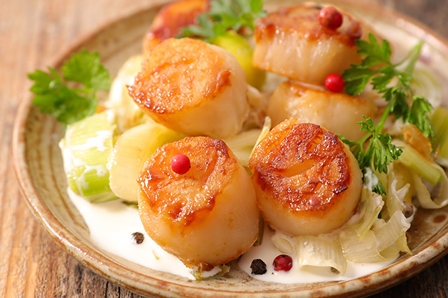 Pétoncles poêlés servis avec poireaux, carottes et champignons sur une sauce à la crème