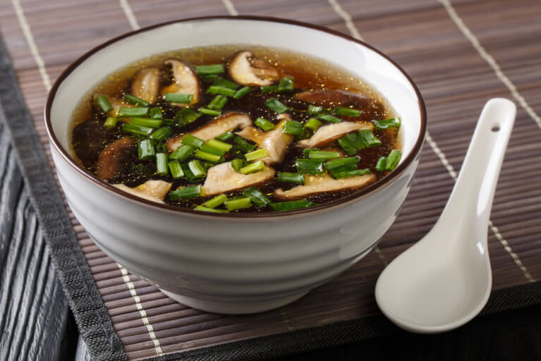 Un bol de soupe avec un bouillon contenant des champignons shiitakes et des poireaux en lanières.