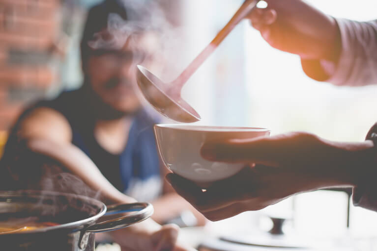 Une femme tenant un bol d'une main et une louche de l'autre pour servir de la soupe.