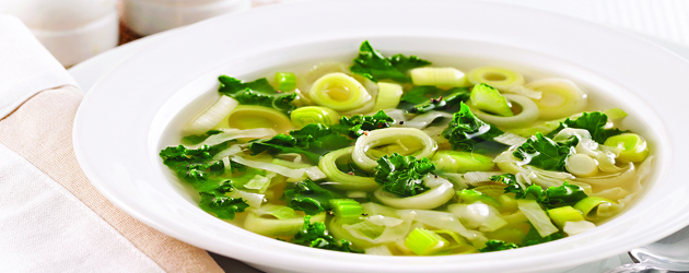 Bol de soupe aux poireaux tranchés, chou vert et chou kale hachés.