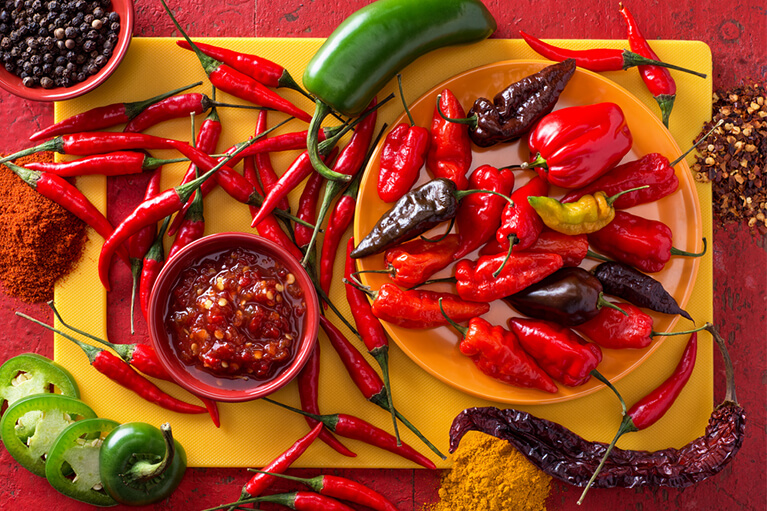 Un petit pot de Sambal Oelek entouré de piments forts rouges pour ajouter du piquant à n’importe quel burger