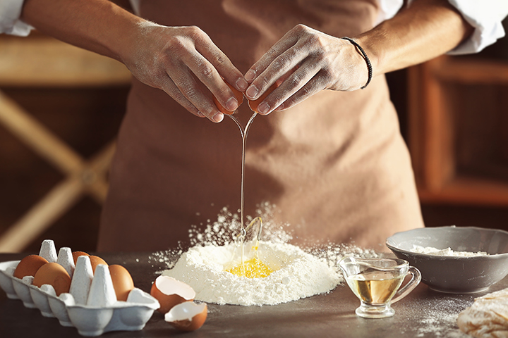 Une personne fait un puits dans la farine et ajoute les œufs pour faire ses pâtes